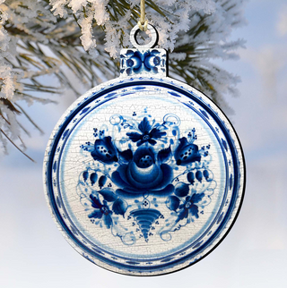 A decorative blue and white ornament with a floral design hangs from a branch against a snowy background.