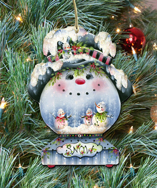 A snowman ornament hanging on a Christmas tree, featuring a snowman, two snowmen, and the word 