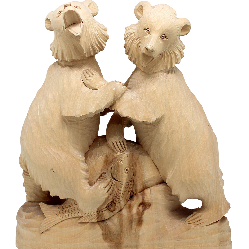 A wooden carving of two bears, one on each side, with fish in their mouths, against a black background.