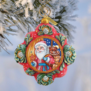 A colorful ornament featuring a smiling Santa Claus figure, a teddy bear, and a star, hanging from a tree branch against a snowy background.