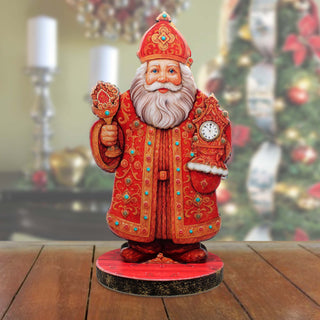 A figurine of Santa Claus wearing a red and gold robe and hat, holding a clock, stands on a red base.