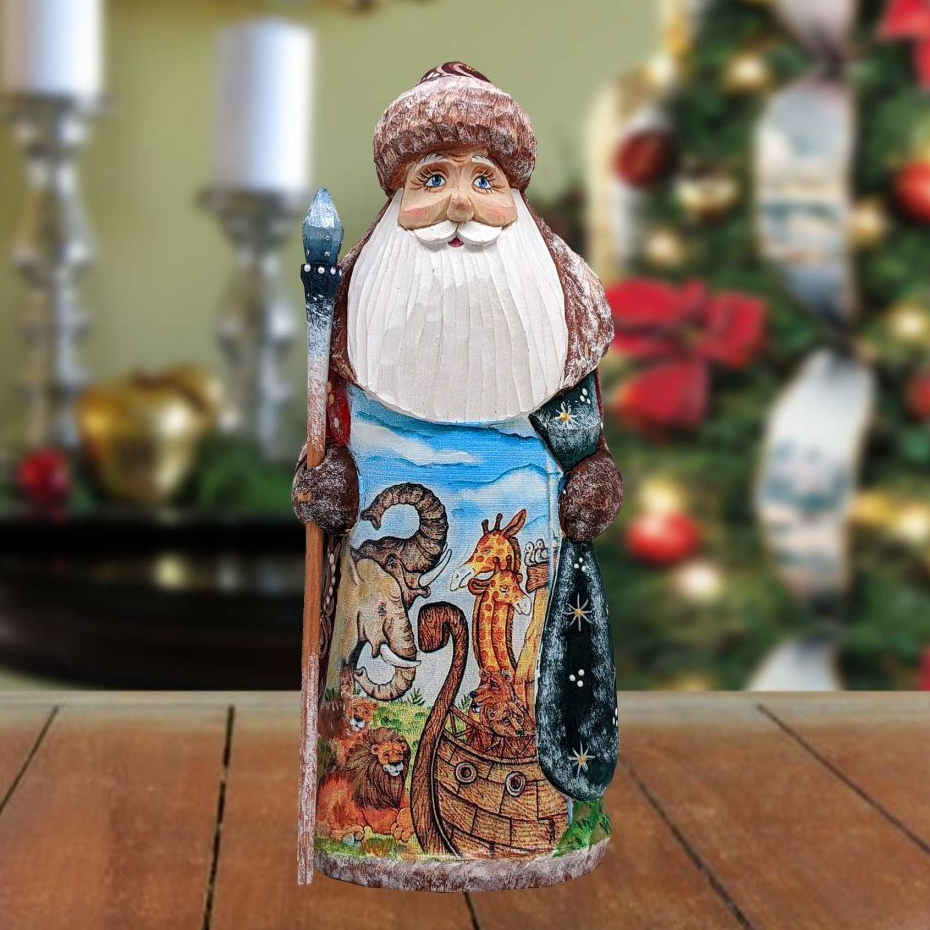 A wooden Santa Claus figurine with a painted design of animals and a boat, standing on a wooden surface in front of a blurred Christmas tree.