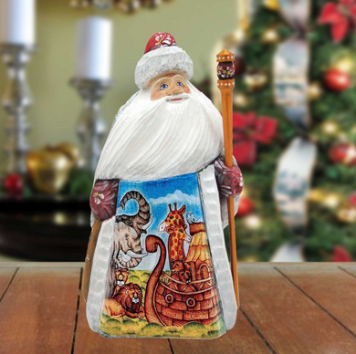 A wooden Santa Claus figurine holding a staff and a decorated nativity scene, with a blurred Christmas tree in the background.