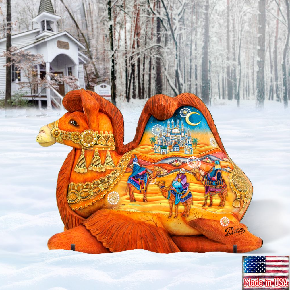 A large, intricately decorated camel sculpture is sitting in the snow, with a snowy landscape and a white building in the background.