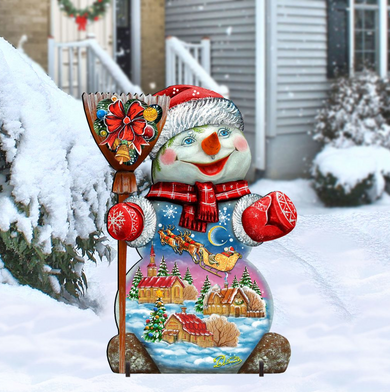 A colorful snowman figure stands in the snow, holding a broom and wearing a red hat and scarf.