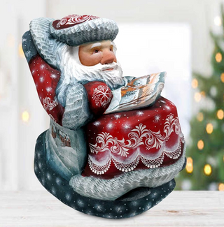 A figurine of Santa Claus sitting in a chair, reading a book, with a snowy background and a Christmas tree in the background.