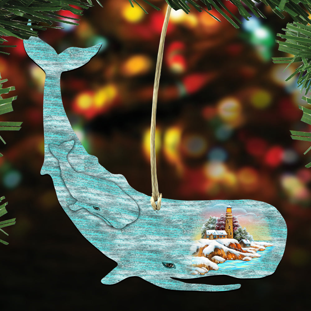 A blue whale ornament with a lighthouse and snowy landscape inside, hanging against a blurred background with colorful lights.